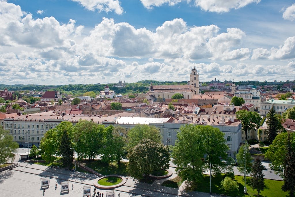역사적인 건물, 교회 타워, 울창한 녹지, 부분적으로 흐린 하늘 아래 광장이 있는 도시의 공중 전망.