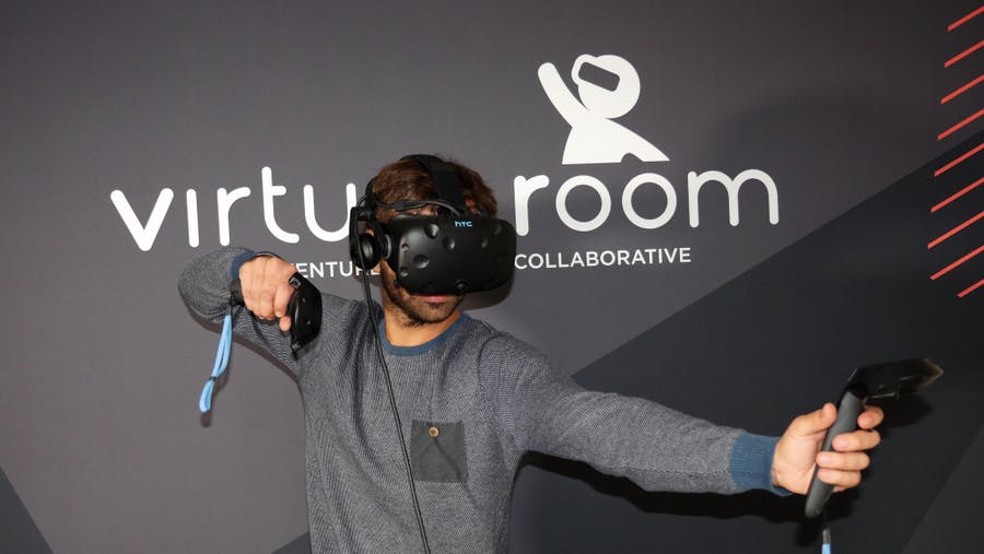가상 현실 헤드셋과 핸드 컨트롤러를 사용하는 사람이 "Virtual Room" 이라는 단어가 적힌 벽 앞에 서 있습니다.