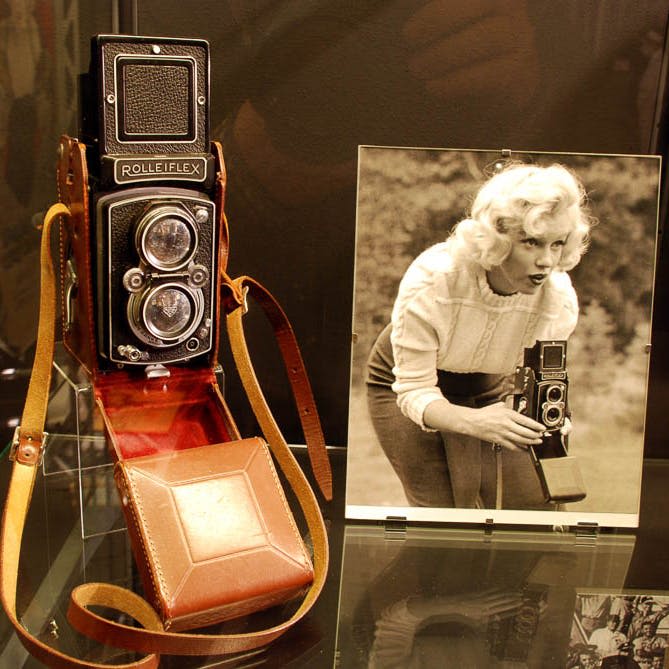 동일한 카메라 모델을 사용하는 여성의 흑백 사진 옆에 빈티지 Rolleiflex 카메라가 표시됩니다.