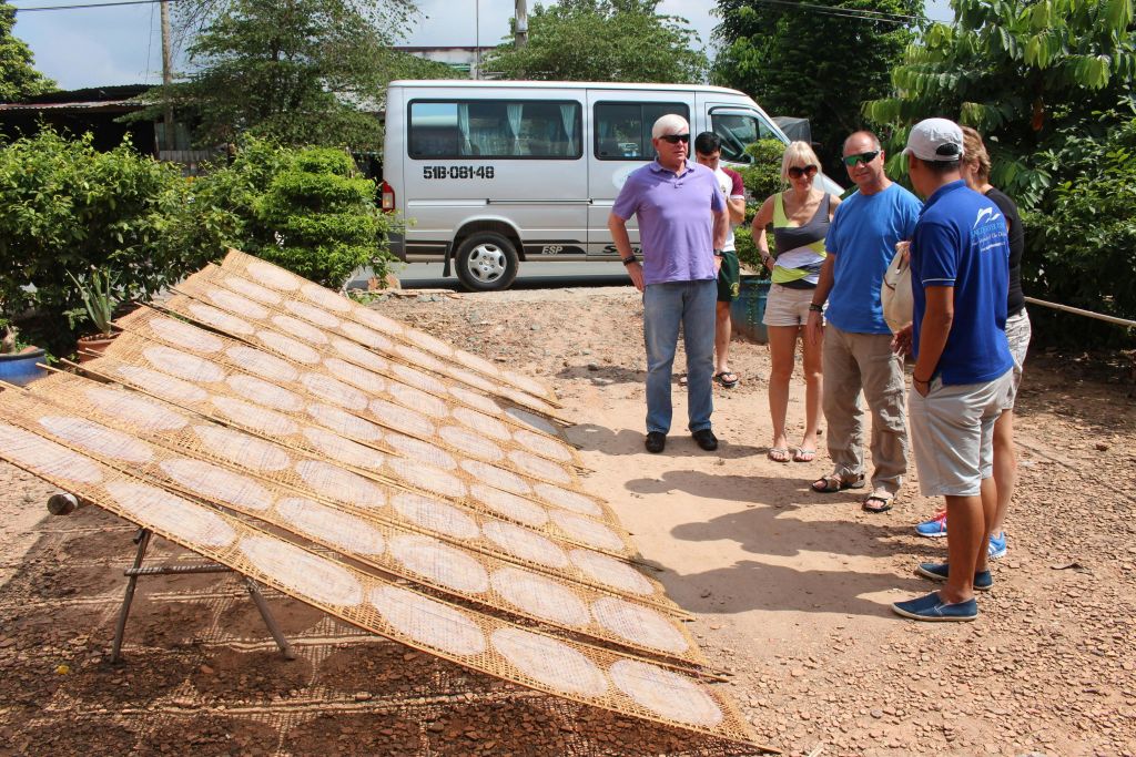 캐주얼한 복장을 한 사람들이 건조대와 주차된 미니밴 근처에 야외에 서 있습니다. 나무가 배경으로 보입니다.