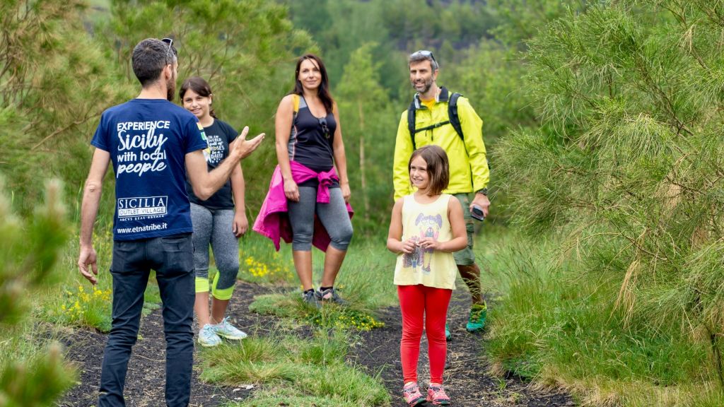 가이드가 나무를 배경으로 잔디가 우거진 산책로에서 어린이를 포함한 4명의 등산객과 웃으며 이야기를 나누고 있습니다.