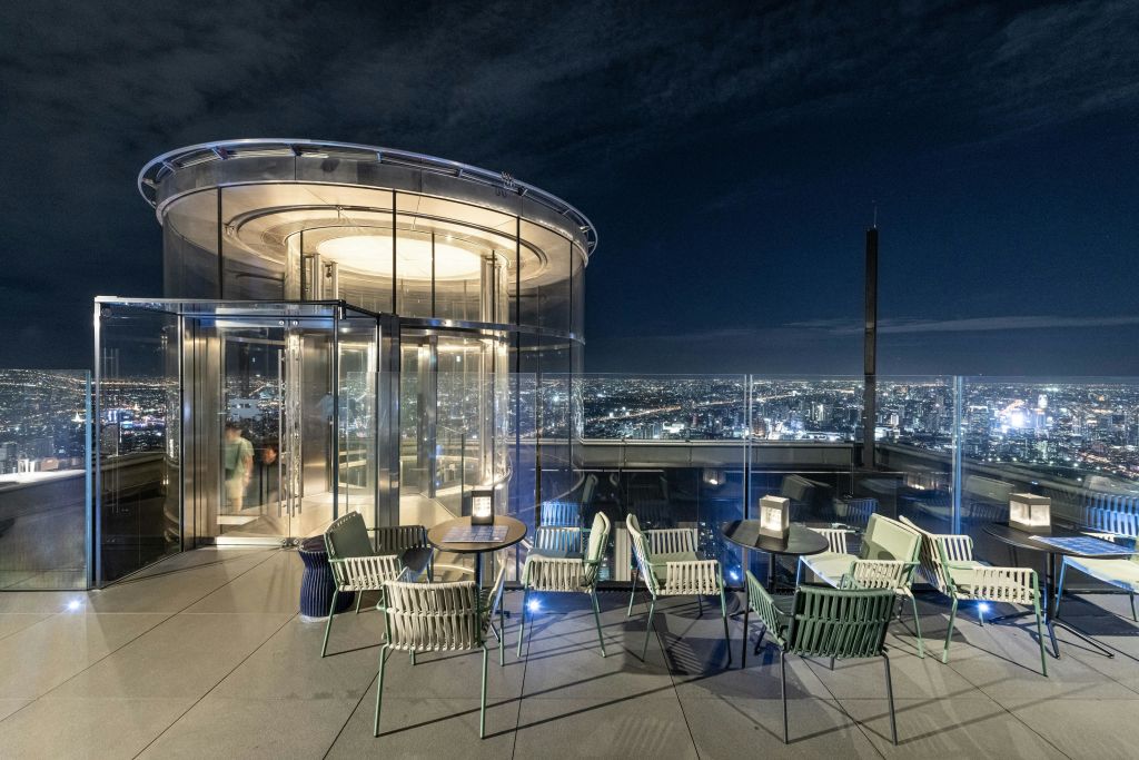 유리 벽, 현대적인 가구, 어두운 하늘 아래 도시의 스카이라인이 보이는 야간 루프탑 라운지.