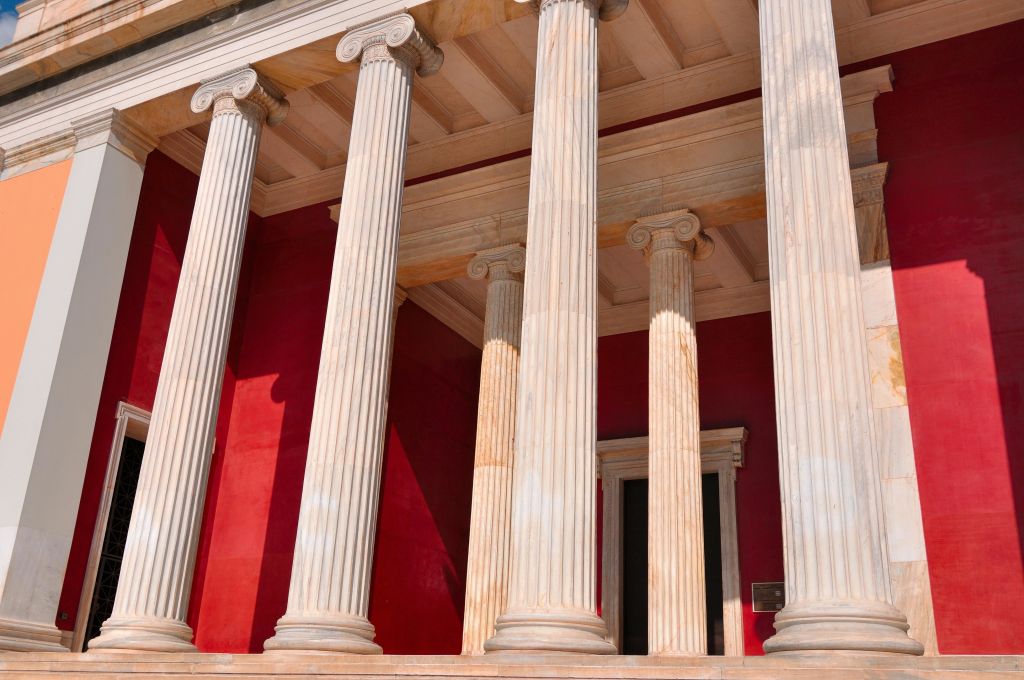 붉은 정면 앞에 고린도 수도가 있는 석조 기둥, 문과 벽면 플라크의 부분적인 모습.