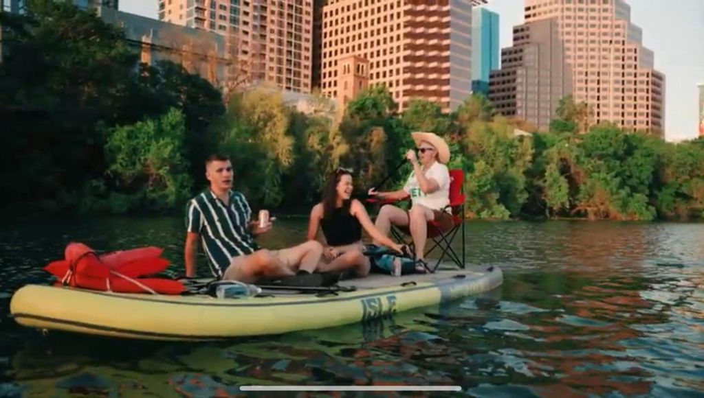 녹지와 건물을 배경으로 한 잔잔한 강가의 패들보드에 앉아 있는 한 무리의 사람들.