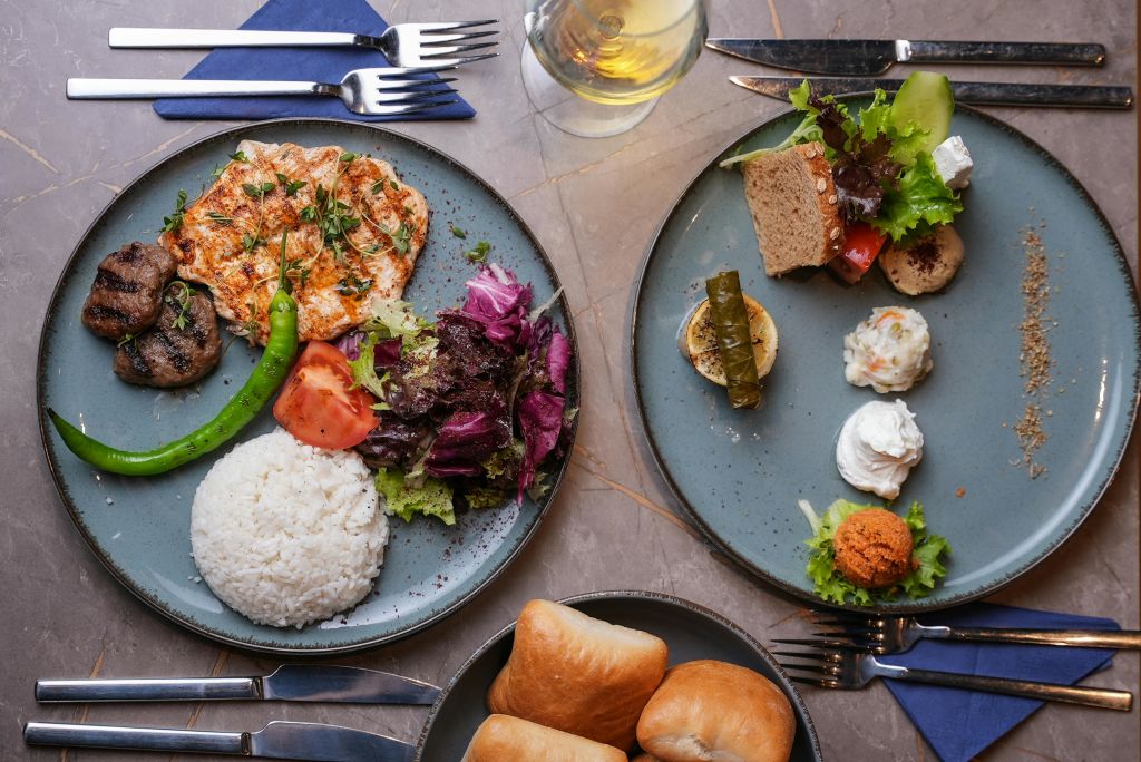 밥, 구운 치킨, 샐러드, 빵, 애피타이저가 담긴 음식 두 접시와 테이블 위에 깔끔하게 정리된 음료와 식기류.