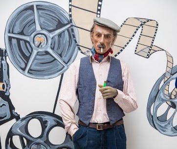 회색 플랫 캡과 조끼를 착용하고 담배를 피우는 남성이 필름 릴과 필름 스트립이 그려진 벽에 서 있습니다.