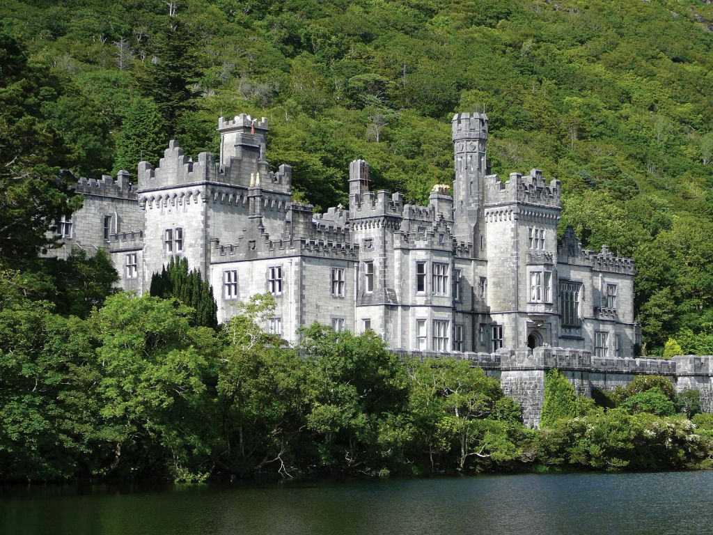 빽빽한 푸른 나무로 둘러싸인 수많은 탑과 화신이 있는 석조 성이 잔잔한 물가에 자리하고 있습니다.