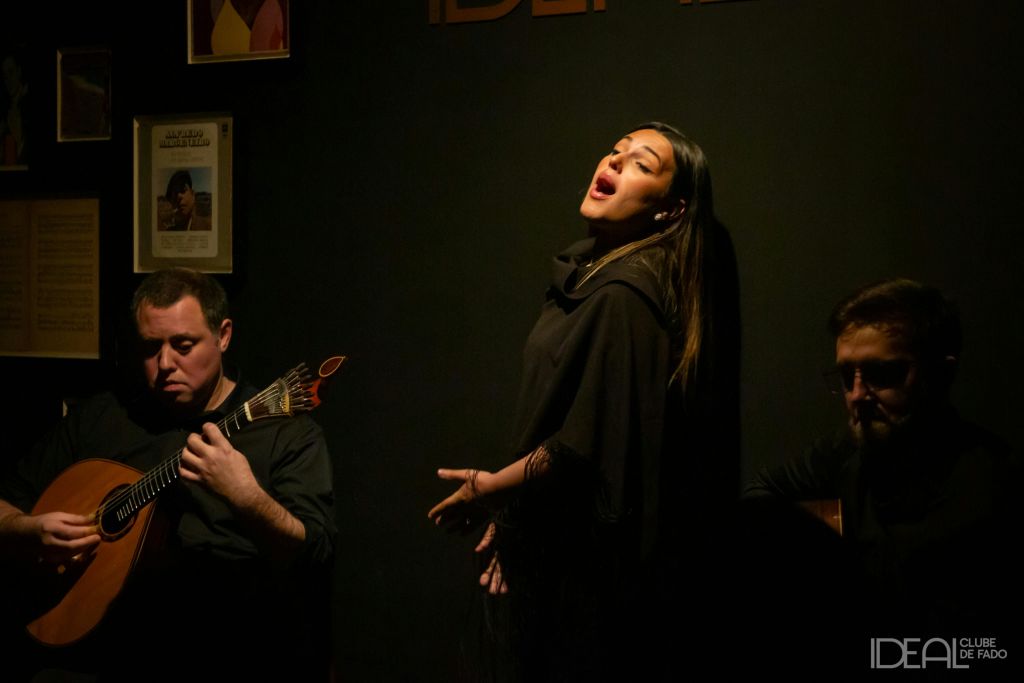 한 여성이 눈을 감고 열정적으로 노래하고, 옆에서 한 남성이 액자 예술로 장식된 어두운 조명으로 꾸며진 방에서 기타를 연주하고 있습니다.