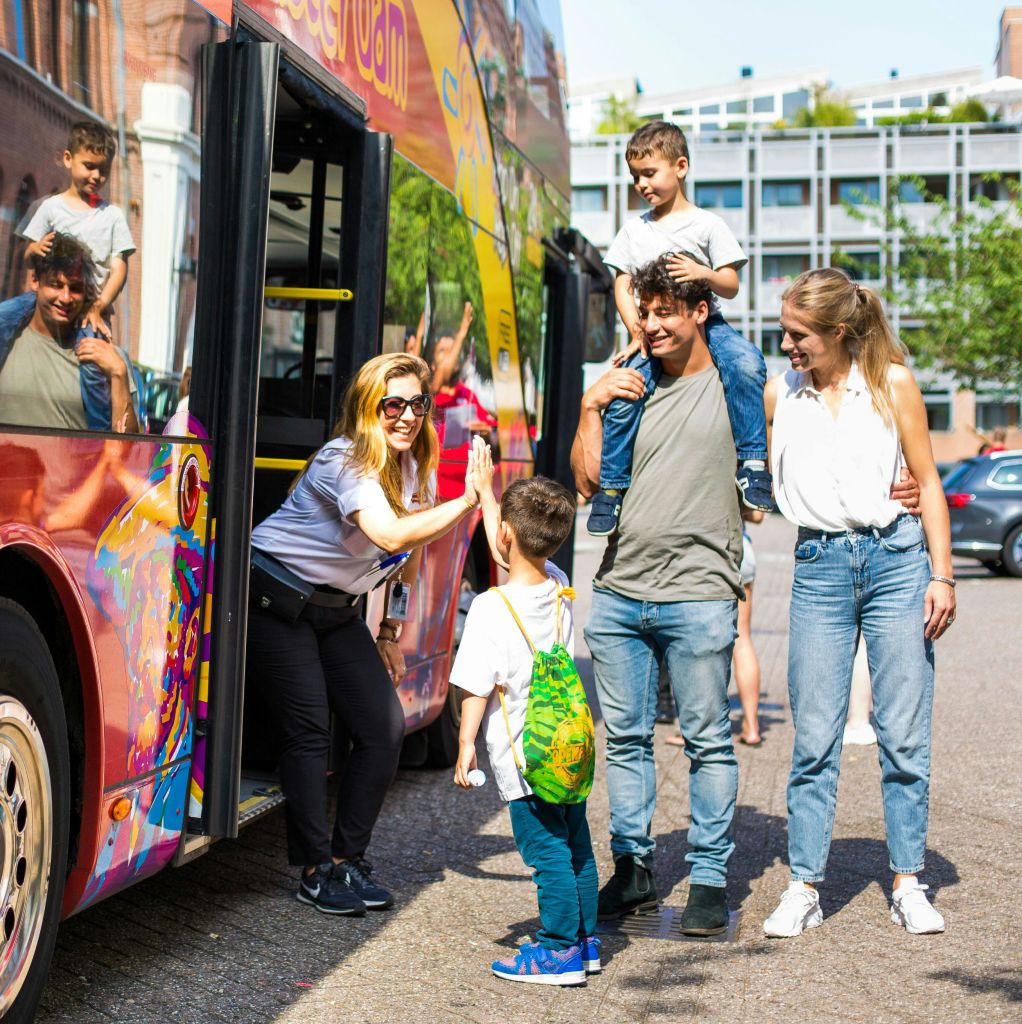형형색색의 버스 근처에서 한 남성이 하이파이브를 하고, 한 남성이 아이를 어깨에 메고, 한 여성이 미소를 짓고 있습니다.