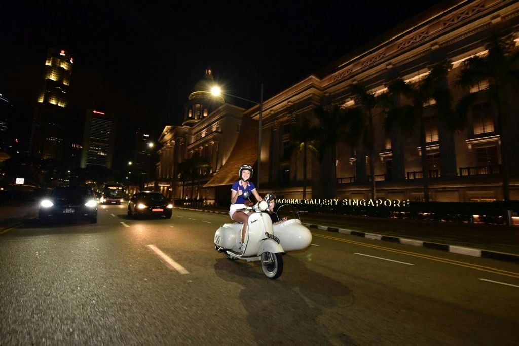 내셔널 갤러리 싱가포르를 배경으로 한 거리에서 밤에 하얀색 스쿠터를 타는 사람.