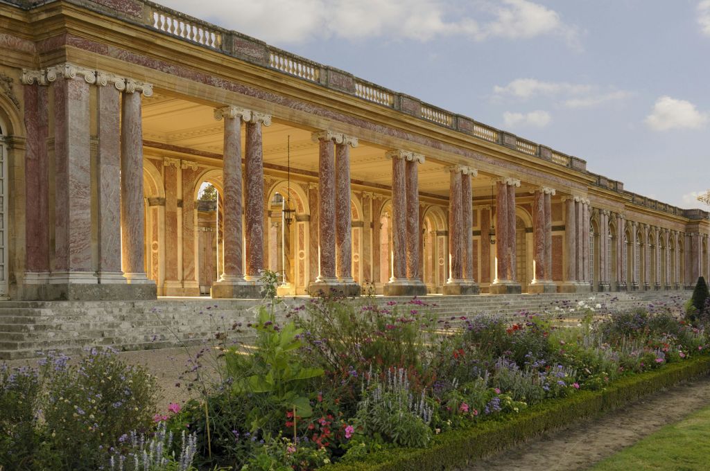 분홍색 대리석 기둥과 아치가 있는 그랜드 콜로네이드로, 활기찬 식물이 있는 잘 손질된 꽃밭과 맞닿아 있습니다.