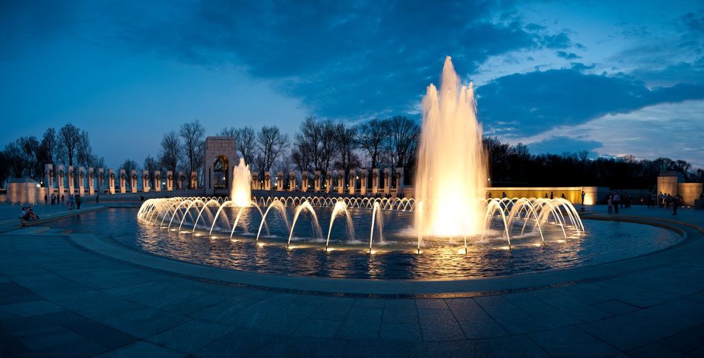 해질 무렵 나무를 배경으로 분수를 밝히고 아치가 있는 건축 구조물을 감상할 수 있습니다.