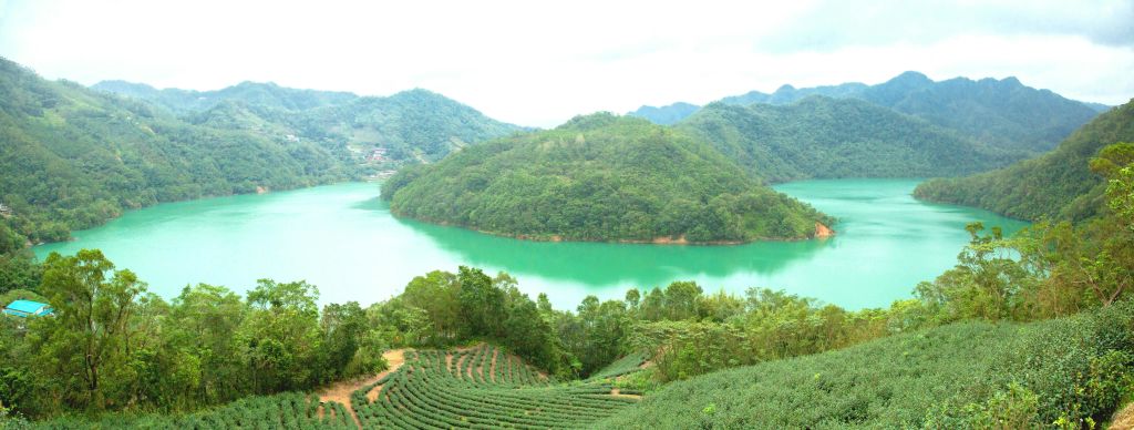 녹음이 우거진 언덕은 흐릿한 하늘 아래 전경에 테라스가 깔린 옥빛 호수를 둘러싸고 있습니다.