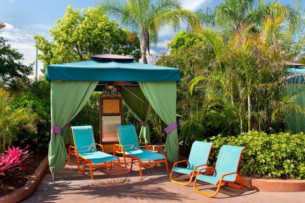 푸른 커튼, 청록색 라운지 의자 4개, 울창한 야자수와 열대 식물로 둘러싸인 풀사이드 카바나.