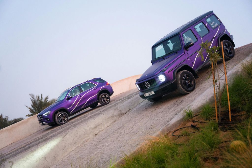 흰색으로 포인트를 준 보라색 SUV 두 대가 경사진 지형을 달립니다. 하나는 오르막길이고 다른 하나는 내리막길입니다.