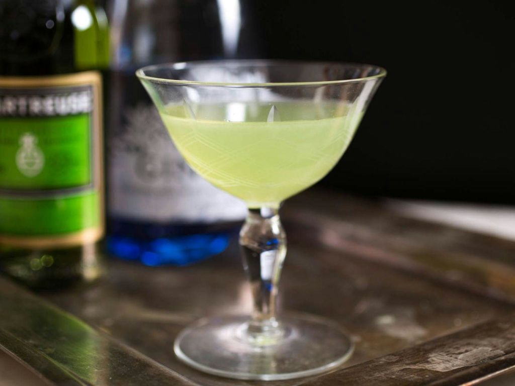 반사 표면에 옅은 녹색 음료를 담은 칵테일 잔으로, 병은 배경이 흐릿합니다.
