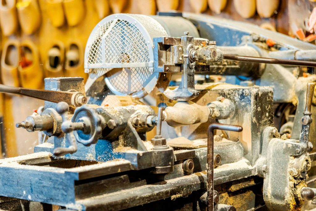 사용 중인 선반 기계의 클로즈업으로 나무 조각을 만듭니다. 목재 부스러기와 먼지가 기계 주위에 퍼져 있습니다.