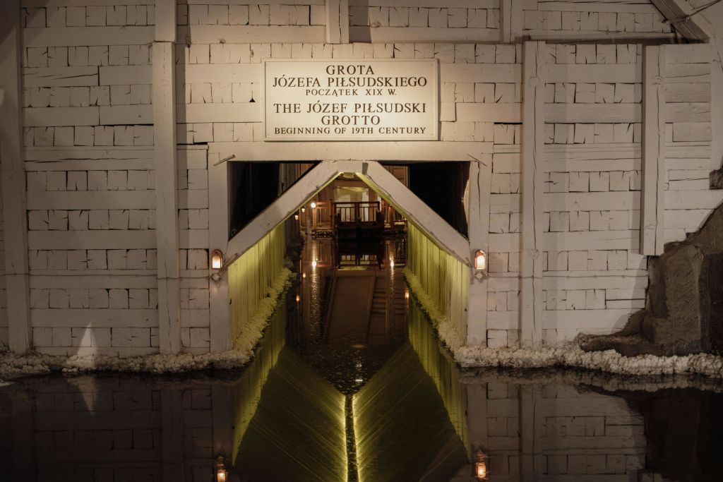 조명 벽이 있는 유제프 피우수트스키 동굴 (Józef Piłsudski Grotto) 입구와 아래 물에 아치형 통로가 반사되어 있습니다.