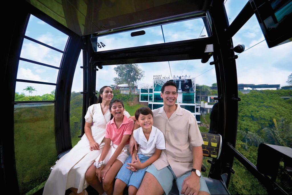언덕과 건물을 배경으로 아름다운 풍경을 감상할 수 있는 케이블카를 탄 네 명의 가족이 웃고 있습니다.