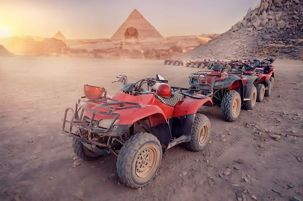 피라미드와 바위 주변을 배경으로 한 사막 풍경에 빨간색 전지형 차량 몇 대가 주차되어 있습니다.