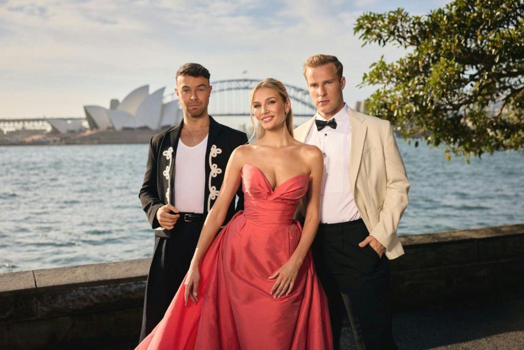 시드니 오페라 하우스와 하버 브리지를 배경으로 야외에서 포즈를 취하는 우아한 옷차림의 세 사람.