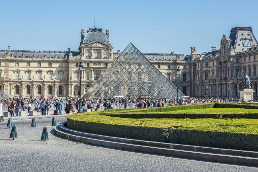 파리의 아름다운 정원과 인파로 둘러싸인 역사적인 건물을 배경으로 한 유리 피라미드.