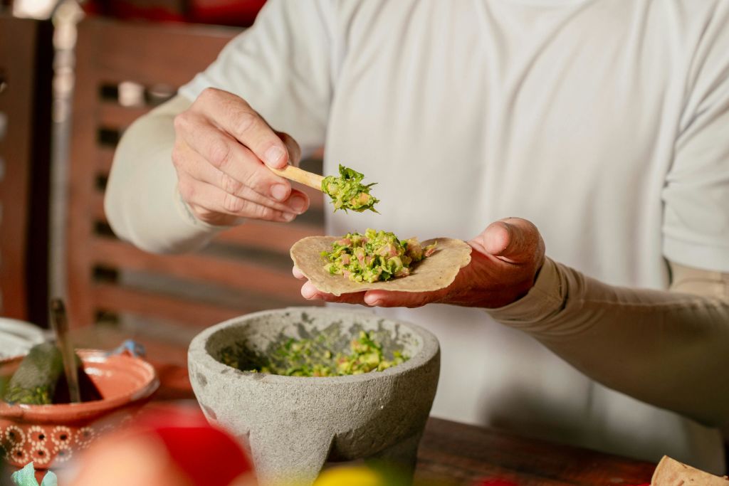 한 사람이 한 손에 또띠아를 들고 나무 숟가락으로 돌 모르타르의 과카몰리를 넣습니다.