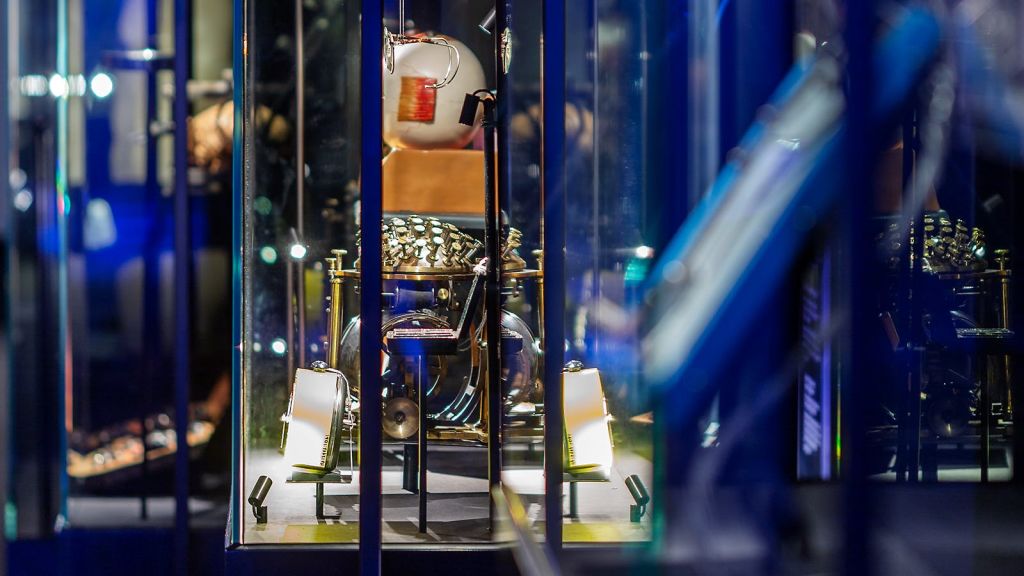 스포트라이트가 비추는 다양한 타악기가 세팅된 빈티지 드럼이 담긴 디스플레이 케이스.