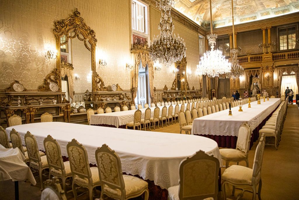 우아한 의자로 둘러싸인 화려한 거울, 샹들리에, 흰색 천으로 덮인 긴 테이블이 있는 호화로운 다이닝 홀.