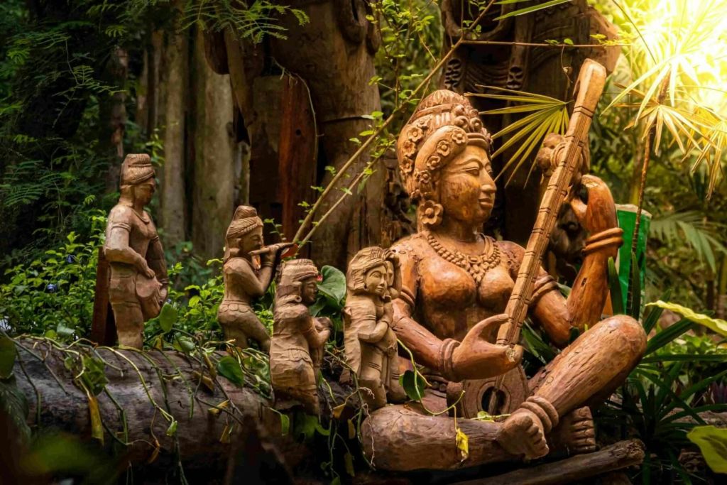 현악기를 연주하는 앉은뱅이 형상의 상세한 나무 조각으로, 울창하고 초록색으로 조각된 작은 형상으로 둘러싸여 있습니다.