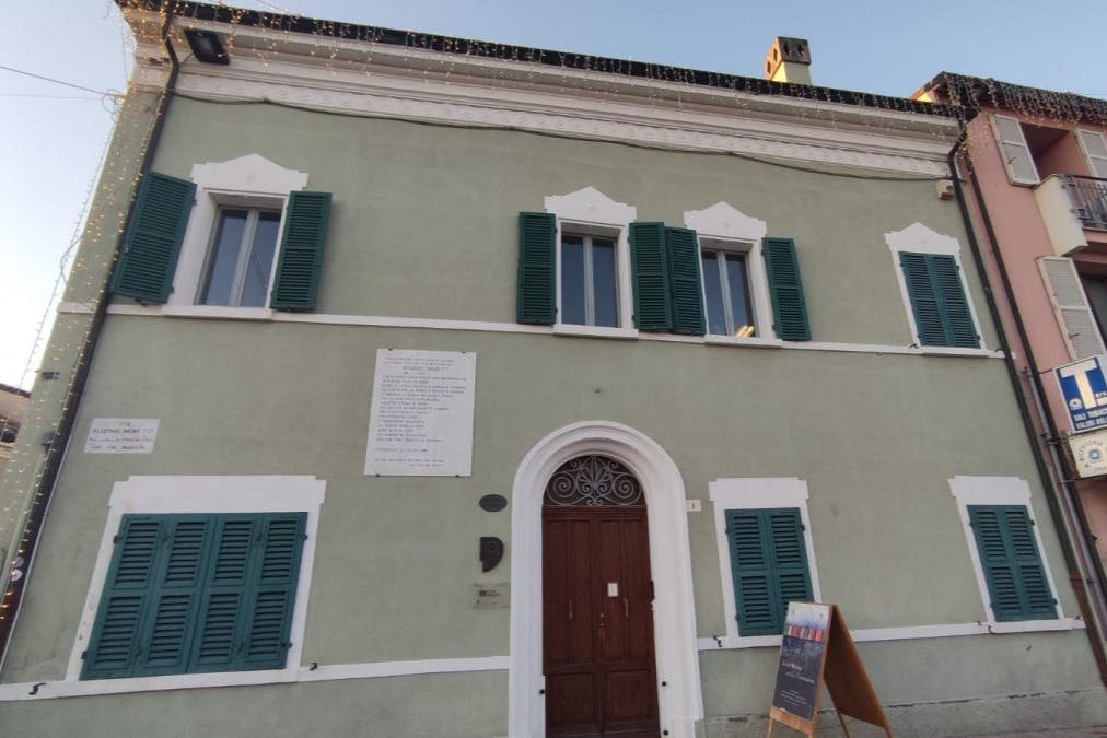 흰색 테두리와 초록색 셔터, 목재 이중 문이 있는 밝은 초록색 건물입니다. 명판과 칠판 표지판이 보입니다.