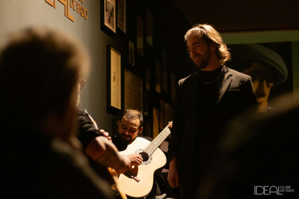 어두운 장식과 액자 예술로 둘러싸인 두 명의 뮤지션이 있는 희미한 조명 객실. 하나는 기타를 연주하고, 다른 하나는 서서 노래를 부를 수 있습니다.