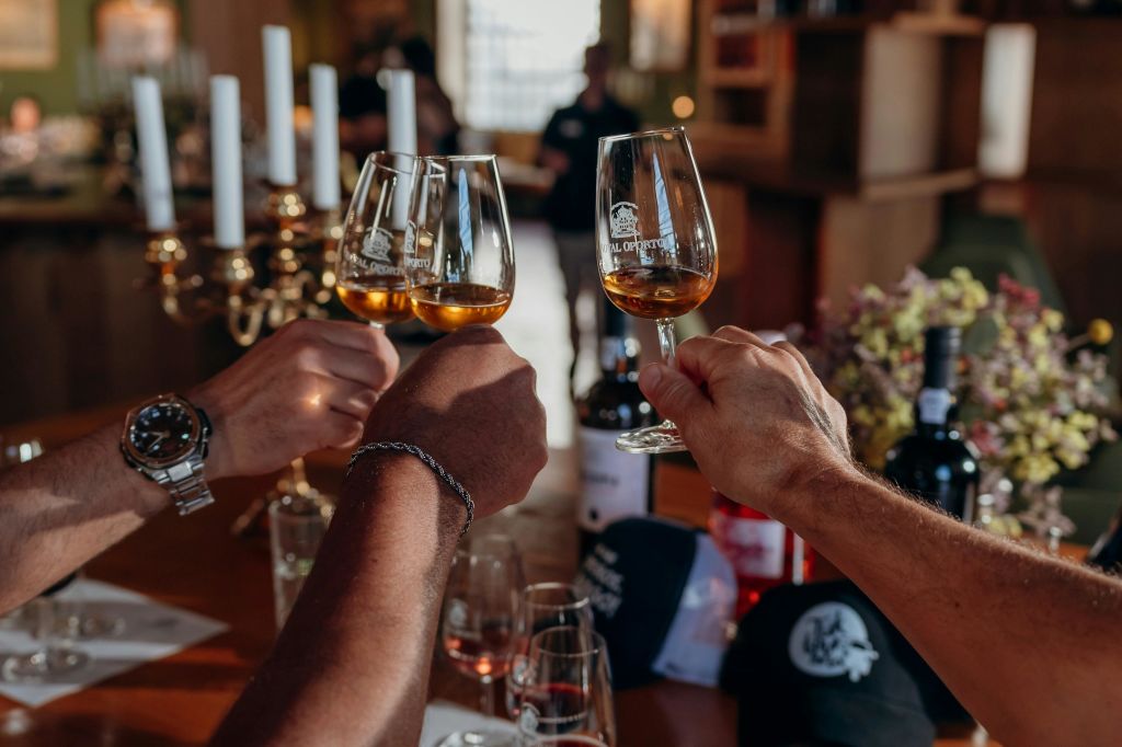 병과 인테리어를 배경으로 따뜻하게 빛나는 방 안의 토스트에서 호박색 와인 잔을 들고 있는 세 손.