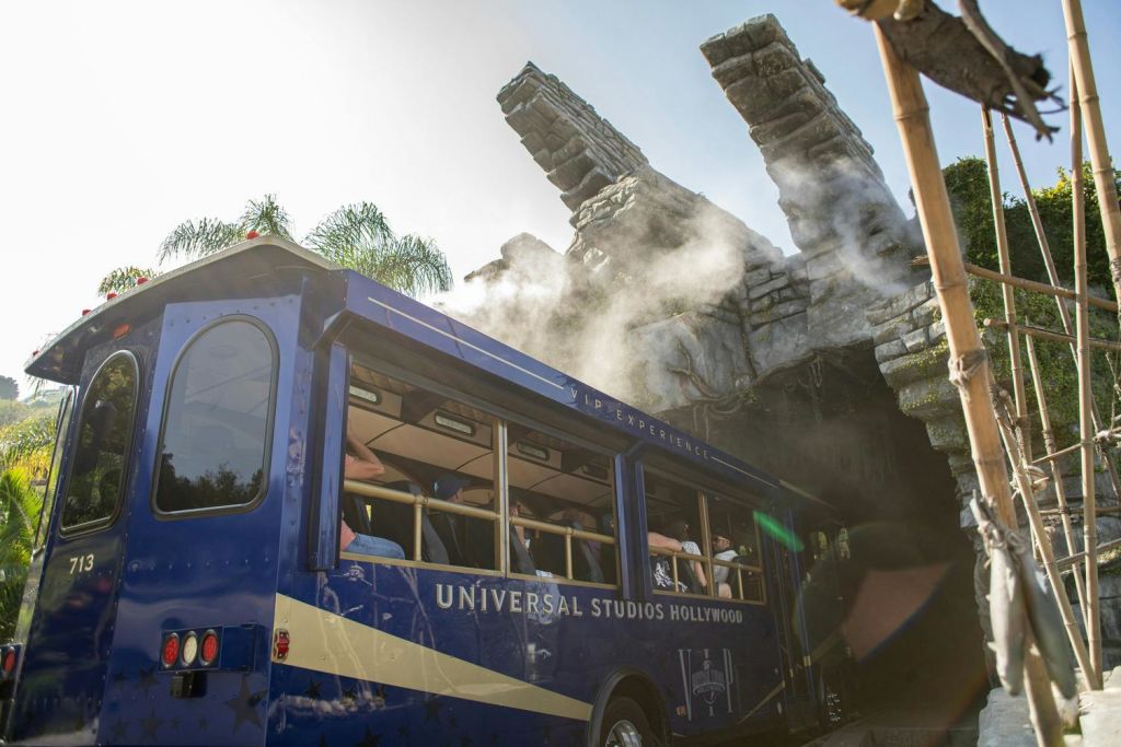 파란 유니버설 스튜디오 할리우드 투어 버스가 밝은 하늘 아래 발톱 모양의 안개 낀 바위를 지나갑니다.