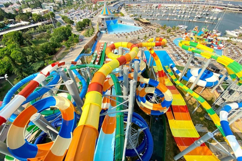 밝은 하늘 아래 여러 개의 미끄럼틀, 수영장, 휴식 공간이 있는 다채로운 워터파크입니다.