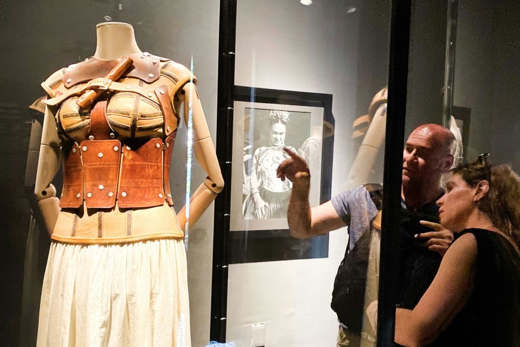 두 사람이 유리 케이스에 담긴 마네킹을 자세히 관찰하고 있으며, 벽면에는 흑백 사진이 전시되어 있습니다.