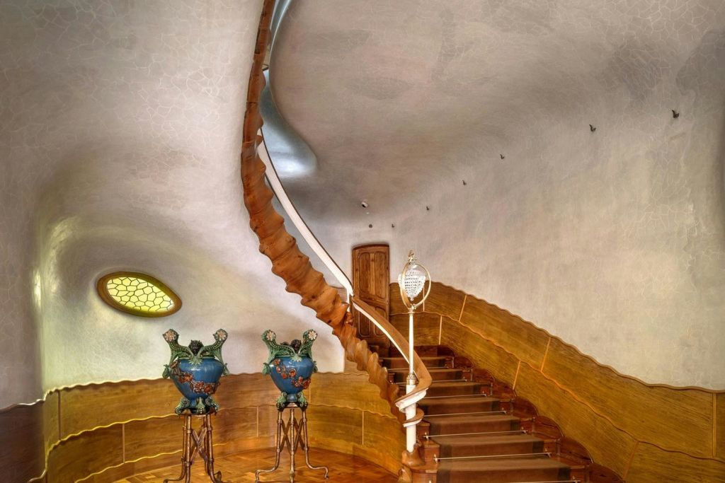 흰색 난간이 있는 곡선형 나무 계단은 나무 문으로 이어집니다. 받침대에는 화려한 장식용 꽃병 두 개가 놓여 있습니다.