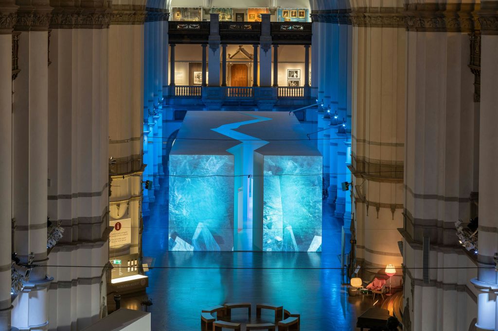 높은 기둥, 파란색 조명, 추상적인 파란색 디자인이 돋보이는 중앙 흰색 구조의 넓은 실내 공간.