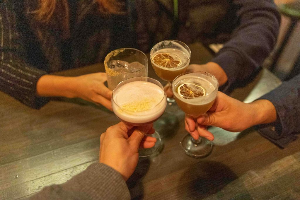 칵테일이 담긴 잔을 들고 나무 테이블 위에서 토스트하는 네 손.