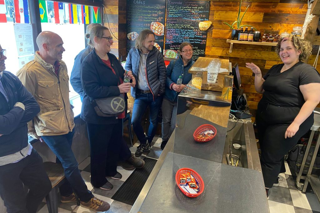 네 명이 카운터에 서서 나무 배경과 칠판 메뉴가 있는 아늑한 카페에서 직원과 웃으며 대화를 나누고 있습니다.