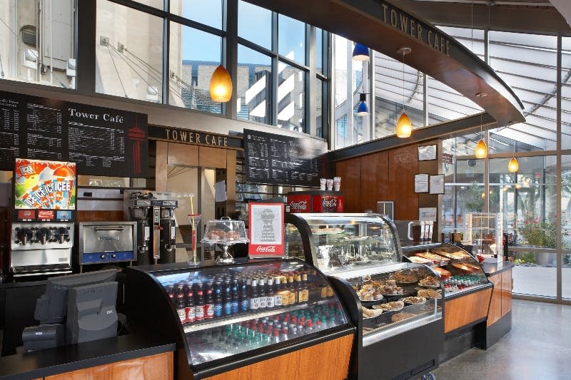 유리창과 매달려 있는 조명이 있는 카페 내부에는 음료수 쿨러, 페이스트리 디스플레이, 머리 위로 놓인 메뉴판이 있습니다.