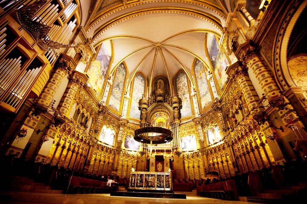 황금색 액센트, 높은 아치형 천장, 복잡한 조각, 스테인드글라스 창문이 있는 웅장하고 화려한 대성당 내부.