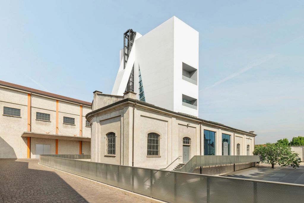 기하학적 구조가 돋보이는 현대적인 흰색 건물은 베이지색의 인더스트리얼 스타일 구조물 뒤에 자리하고 있으며, 창문을 가로막고 있습니다.