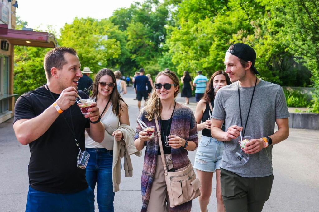선글라스를 쓴 사람들 중 일부는 햇볕이 쨍쨍한 날 야외에서 걷고 컵으로 음식을 즐기고 있습니다. 나무는 배경에 있습니다.