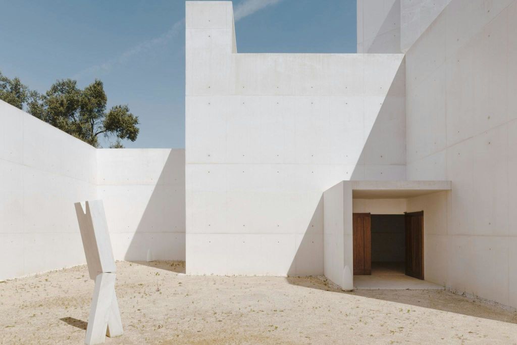 기하학적 모양과 그림자, 열린 출입구, 맑고 푸른 하늘 아래 희박한 나무가 있는 미니멀한 흰색 콘크리트 건물.