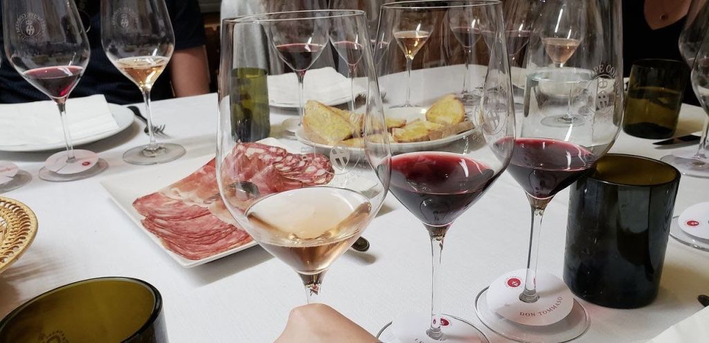 와인잔이 놓인 테이블의 클로즈업, 잘게 썬 고기 한 접시, 얇게 썬 빵 한 접시. 전경에 와인잔을 들고 있는 손.