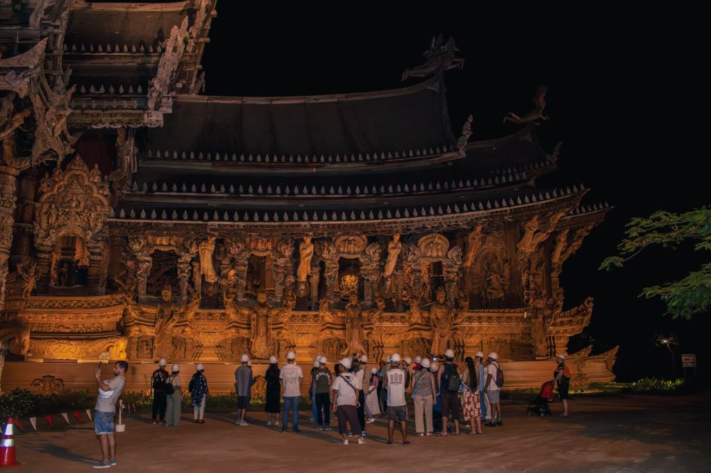 하얀 모자를 쓴 사람들이 밤에 정교하게 조각된 사원을 관찰하고 있습니다.