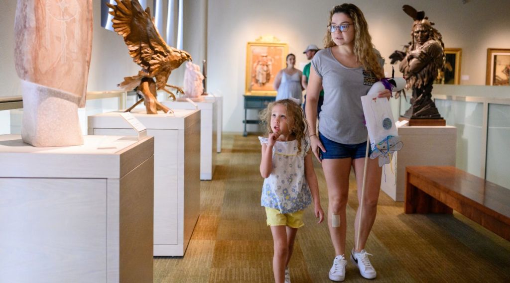 한 여성과 어린이가 미술관을 거닐고 있습니다. 벽에는 조각품과 액자에 담긴 예술품으로 둘러싸여 있습니다.