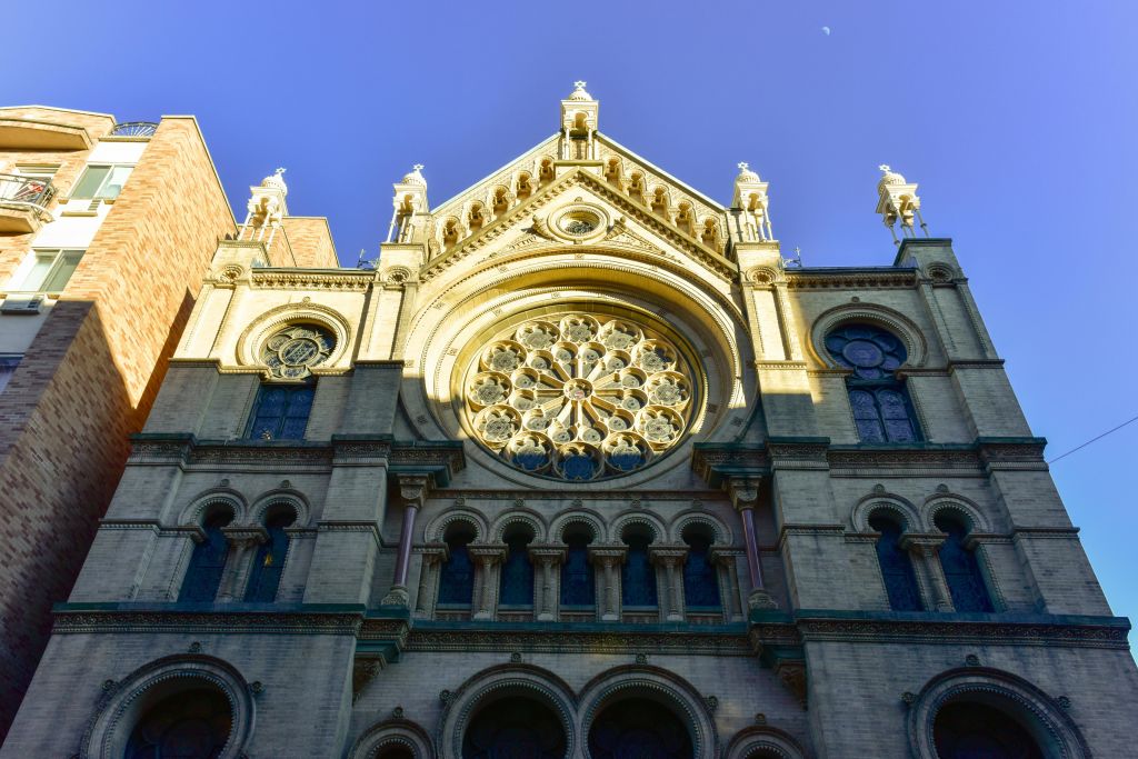 커다란 원형 스테인드글라스 창문과 맑고 푸른 하늘을 배경으로 한 정교한 건축 디테일이 돋보이는 고딕 양식의 건물 외관.