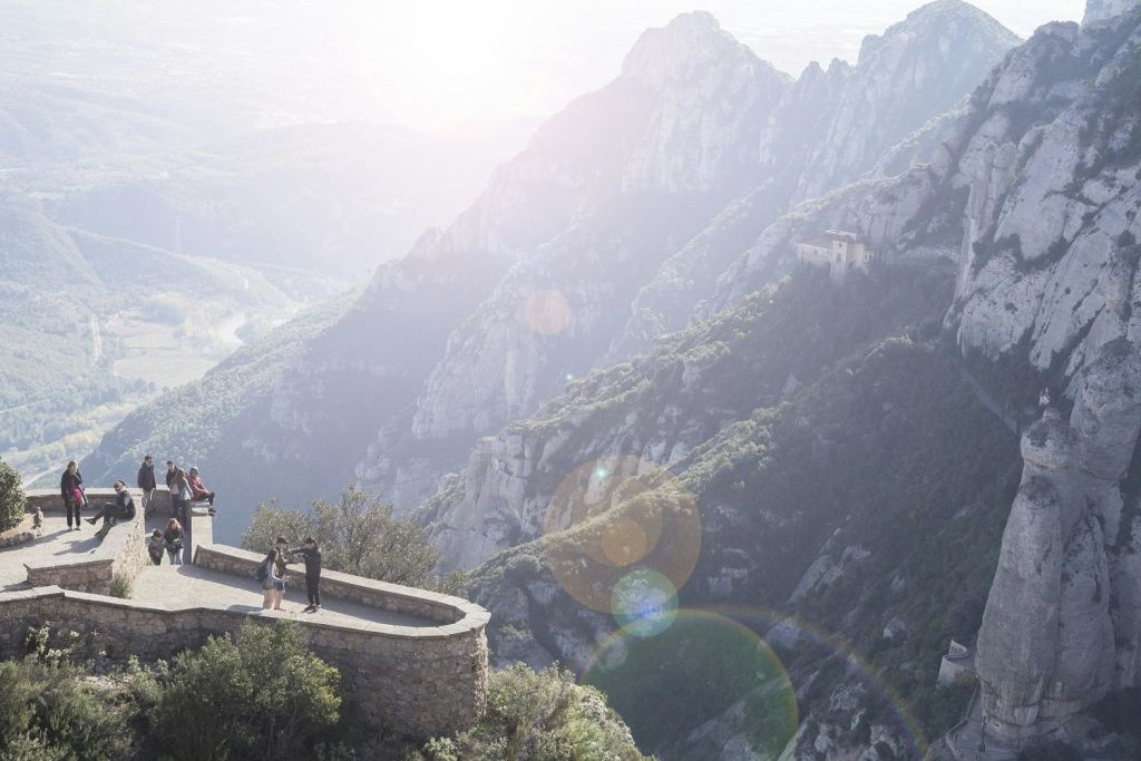 가파른 절벽과 먼 건물이 있는 산 풍경이 내려다보이는 석조 플랫폼에 두 사람이 서 있습니다.